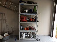 Full view of white plastic storage shelf with five shelves assembled in garage. Contains various items not included.