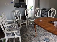 Six white wooden dining chairs around a wooden table, 2 with armrests and 4 without. Upholstered seats with floral fabric visible.