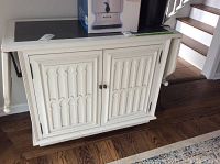 Front view of white wooden sideboard with two drop leaf sides, carved panel doors, and black top surface with items on top.