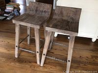 Front view of both wooden stools showing low backs and twisted metal footrests