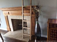 Decorative wooden ladder leaning against a fireplace and recycled glass vase with dried floral arrangement beside it.