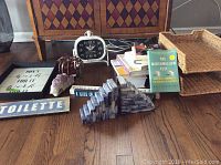 Overview showing wooden signs, framed print, books, untested clock, wicker desk organizer, amethyst crystal rock, and decorative pyramid sculpture on wooden floor in front of a cabinet.