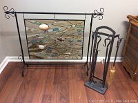 Full shot of fireplace screen with wave pattern multicolor glass and seashells plus wrought iron fireplace tool set on floor.