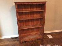 Front view of the antique wooden bookcase showing four shelves and paneled back.