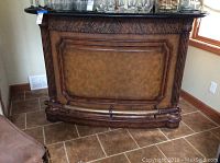 Full view of the stone top bar showing wood and leather front panel with decorative carved legs and foot rail.