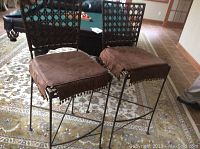 Pair of metal framed bar stools with rattan backs and brown microfiber cushions with tassels on a patterned rug.