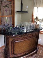 Wide shot showing entire assortment of barware and glassware on curved wooden bar counter.