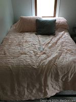 Full view of bed made with peach-colored linens and green throw pillow against window