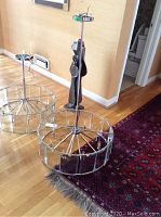 Full view of chrome ceiling fixture standing on wooden floor next to rug and wall, showing the circular frame and central pole.
