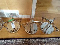 Front view of three chrome ceiling fixtures laid on the floor with mirrored round bases and triangular chrome frames.