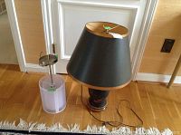 Two lamps on wooden floor against door: one table lamp with black and gold lampshade and one modern cylindrical ceiling fixture lamp