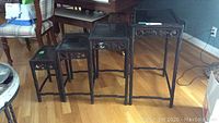 All four black carved wood nesting tables nested together showing carved scroll and leaf patterns on the apron sides.