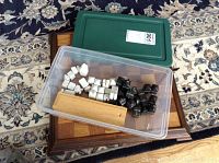 Plastic container holding white and black alabaster chess pieces on top of a wooden chess board on a patterned carpet.