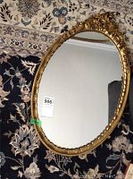 Full view of the oval ornate gold frame wall mirror placed on a patterned rug showing the overall item.