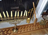 Wide view showing the brass menorah candelabra with eight candles, brass fireplace tools including broom and shovel, and brass andirons near the fireplace