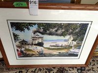 Framed print in wood frame with a scenic lakeside view, boat, people, cars, and buildings.
