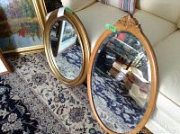 Two mirrors placed on carpet in front of sofa. One round with gold frame, one oval wooden with carving.