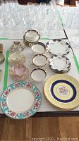 Full overview of cups, plates, and glassware arranged on table showing various vintage china and glassware pieces.