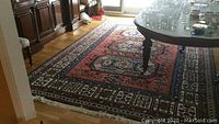 Full view of large red geometric medallion wool rug laid in dining room