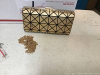 Front view of gold clutch with black geometric pattern and gold chain strap.