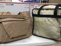 Beige CATO purse with chainlink feature next to clear Homewood Suites tote on white surface