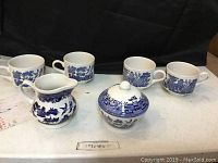 Photo showing the full set of 7 tea set pieces, including 4 tea cups, creamer jug, sugar bowl with lid, and sugar dish bowl, all featuring blue and white Willow pattern.