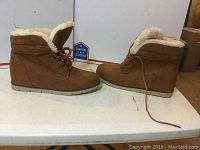 Side profile of pair of brown Wendy Girl booties with fur lining and laces, showing the lace-up detail and flat sole with slight heel.