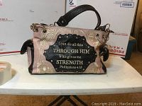 Front side view of the pink and brown handbag displaying Bible scripture and floral embossing.