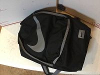 Front view of Nike black backpack with large gray swoosh logo and zippered front pocket