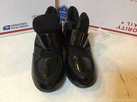 Front view of the black patent leather shoes showing glossy finish and velcro straps.