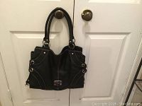 Front view of the Nine West black shoulder tote bag hanging on double door knobs, showing the bag's size, shape, and dual handles.