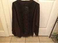 Photo of a brown men's sweater with a geometric triangular pattern on the front, hanging on a hanger in front of a door.