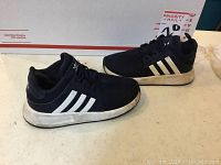 Side view of both Adidas black and white kids sneakers, size 9K, showing general condition and minor dirt on sole.