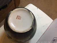 Bottom view of large dark ceramic vase showing red Chinese seal mark and signs of wear on foot ring.