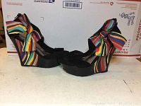 Pair of black platform wedge heels with rainbow striped bows, side view showing profile and height of heel.