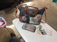Front view of the Nicole Lee denim jeans handbag and matching wallet on a white table showing the design and attached tags.