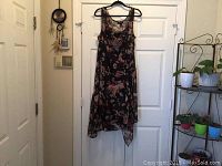 Full view of the floral patterned sleeveless dress hanging on door showing the asymmetrical hem and sheer fabric overlay.
