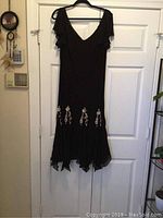 Full front view of the black off shoulder dress showing v neckline, short flutter sleeves and rose embellished bottom.