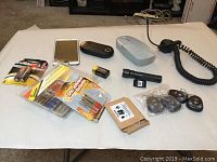 Photo showing damaged Samsung Galaxy Note 3, Helio phone, car remotes, battery packs, universal car charger, flashlight, and various small accessories on white surface.