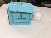 Light blue rectangular Lladro box with ornamental blue border design and logo. Bell ornament is beside the box on a white surface.