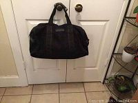 Photo of black soft leather bag hanging on door knobs, showing front and side angles, highlighting its shape and handle structure.