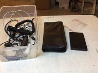 Plastic container with various USB cables and cords, black zippered carrying case, and external hard drive on table.