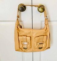 Front view of the beige Michael Kors purse showing two front pockets with buckle closures.