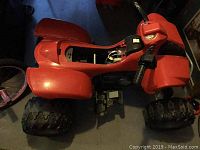 Red kids ride on battery ATV showing underside and battery compartment area