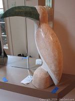 Front and side view of the large marble toucan statue positioned on a shelf with a mirror behind it.