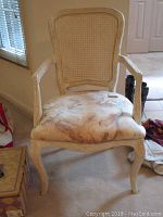 Front view of the cream painted wood armchair with caned back and upholstered abstract seat.