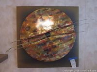 Front view of the round iridized metal wall plaque showing multi-toned metallic colors and sculptural design element crossing the plaque.