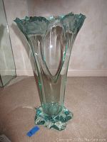 Clear view of the aqua blown crystal vase showing sculptural abstract form and ruffled edges on top, standing on carpeted floor against wall.