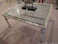 Front angled view of the metal cocktail table with inset glass square top, showing full table and legs.
