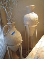 Two stone textured ceramic urns on metal stands side by side, showing overall condition and texture.